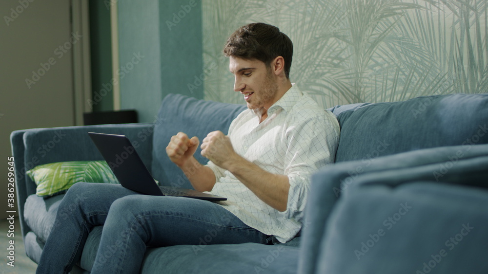 Successful guy receiving message laptop indoors. Happy man doing winner gesture