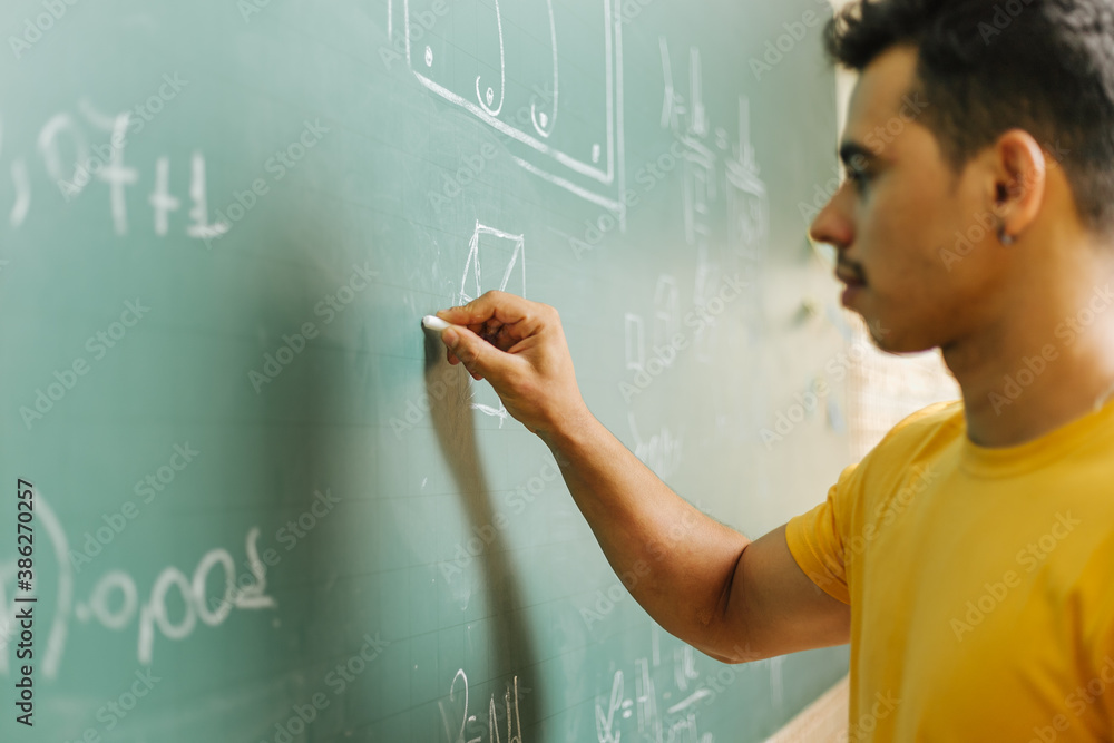 Latin student in the classroom. Man student writing assignments on blackboard during class Latin student in the classroom. Man student writing assignments on blackboard during class