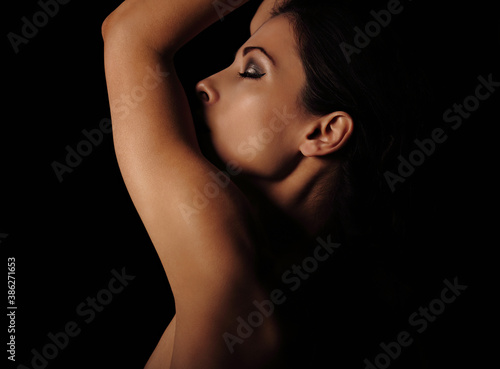 Beautiful mysterious woman in darkness with closed eyes in shadows on dramatic  black background with empty copy space. Closeup