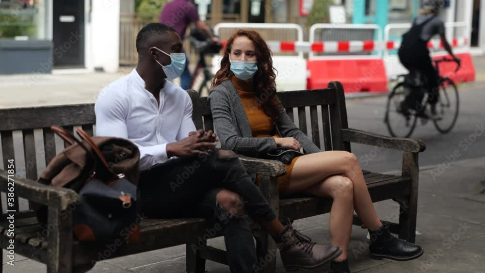 Couple sitting on bench chatting with face masks Couple sitting on bench chatting with face masks