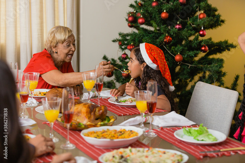 Summer Christmas dinner in Brazil. Real Brazilian family having fun at the Latin American Christmas party. elderly woman giving dinner in the mouth of a curly haired child