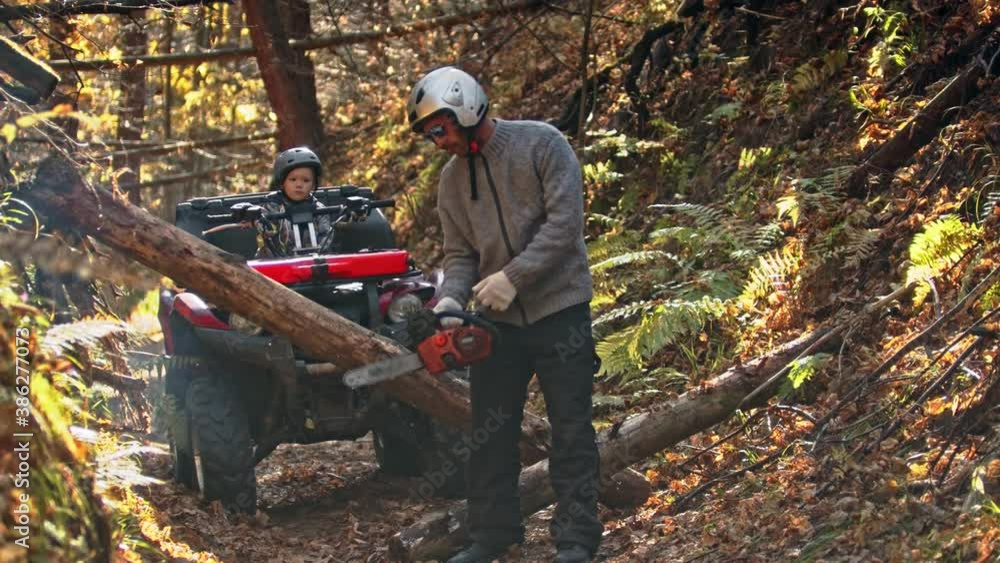 An autumn forest - man turns on a chainsaw in the woods and his son is waiting for him on a quad bike An autumn forest - man turns on a chainsaw in the woods and his son is waiting for him on a quad bike