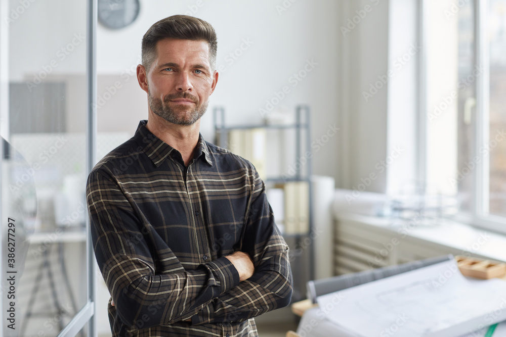 Waist up portrait of confident bearded architect looking at camera while standing with arms crossed by drawing desk in office, copy space Waist up portrait of confident bearded architect looking at camera while standing with arms crossed by drawing desk in office, copy space