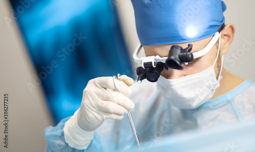 Fotografia male neurosurgeon uses surgical instruments in binocular glasses with microscope lenses operates in a modern operating room