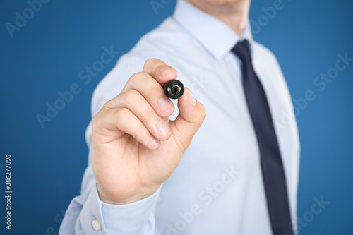 Businessman with marker against blue background, focus on hand