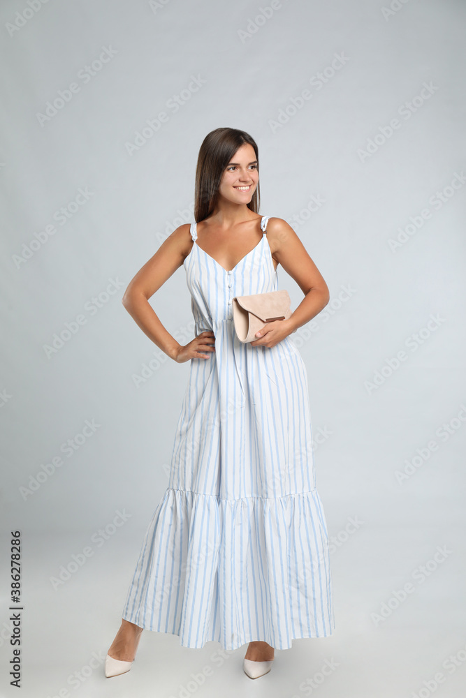 Young woman wearing stylish dress with elegant clutch on light grey background Young woman wearing stylish dress with elegant clutch on light grey background