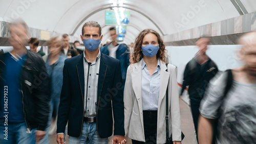 man and a woman in protective masks walking along the platform in subway .