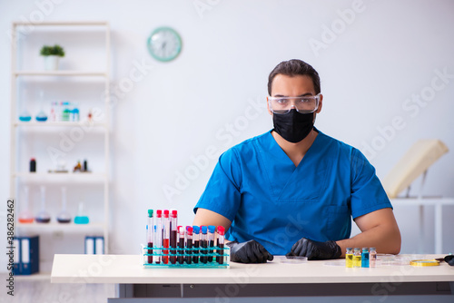 Young male biochemist testing blood samples in pandemic concept