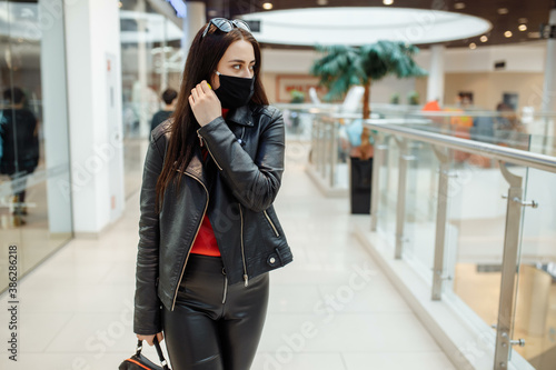 A girl with a medical black mask is walking along a shopping center. Coronavirus pandemic. A girl in a protective mask is shopping at the mall