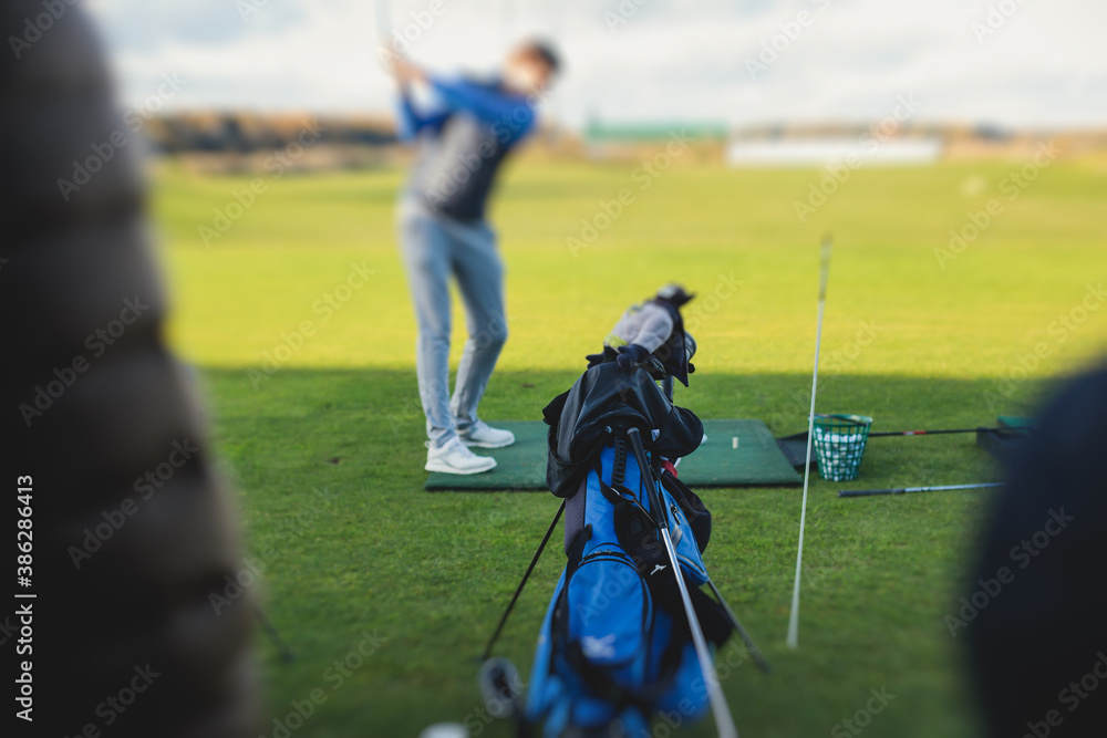 Group of golfers practicing and training golf swing on driving range practice, men playing on golf course, golf ball at golfing complex club resort Group of golfers practicing and training golf swing on driving range practice, men playing on golf course, golf ball at golfing complex club resort