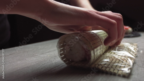 Cropped anonymous cook hands with rolling fresh sushi with bamboo mat while working in authentic Japanese restaurant,Close-up of chef's hands rolling a sushi roll on bamboo mat.Sushi making process