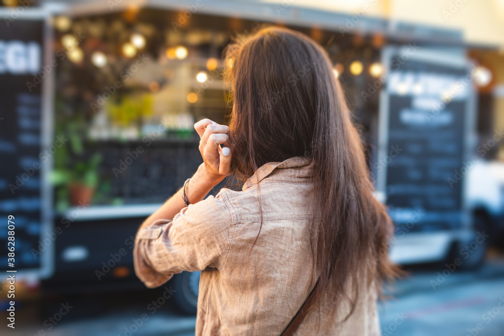 Fototapeta premium Girl ordering street food in colourful food truck van on food festival, summer sunny day