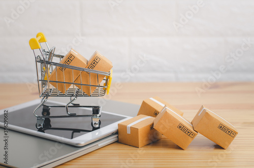 Brown paper boxs in a shopping cart with tablet on wood table in office background.Easy shopping with finger tips for consumers.Online shopping and delivery service concept.