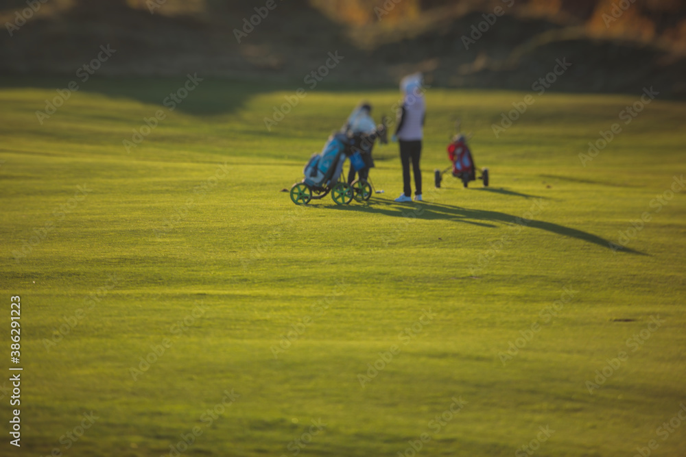 Vibrant view of golf course in countryside, landscape field with with a rich green turf and sand bunkers summer sunny day, a group of golfers walking and playing Vibrant view of golf course in countryside, landscape field with with a rich green turf and sand bunkers summer sunny day, a group of golfers walking and playing