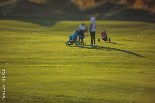 Vibrant view of golf course in countryside, landscape field with with a rich green turf and sand bunkers summer sunny day, a group of golfers walking and playing