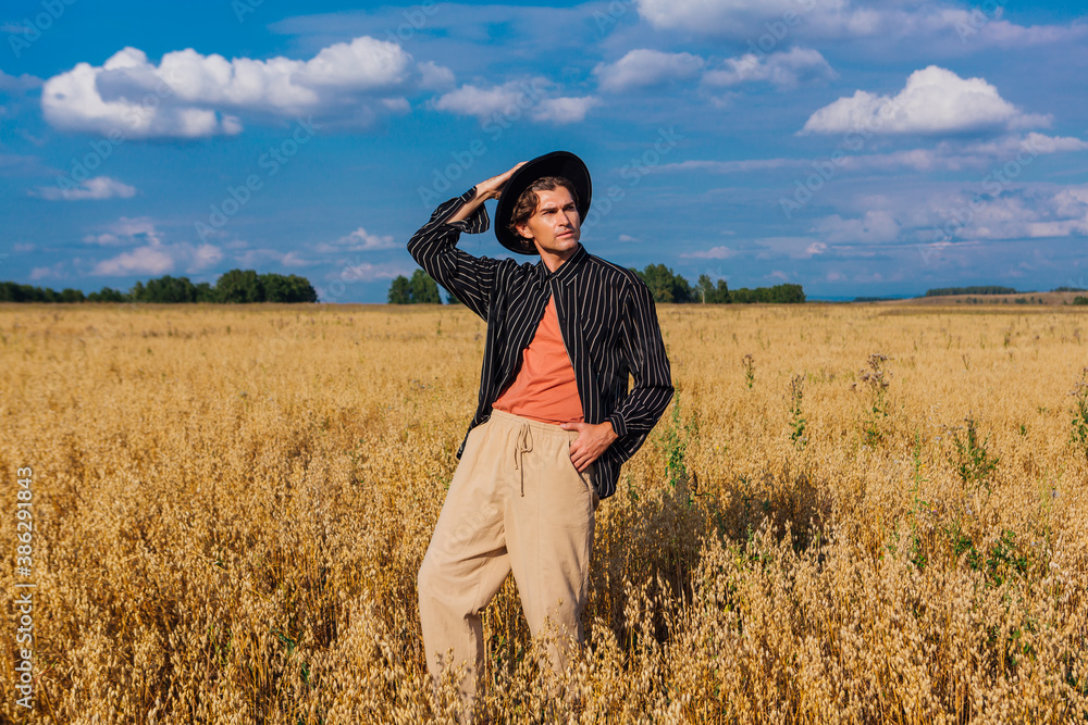 Tall handsome man with black hat standing at golden oat field. Tall handsome man with black hat standing at golden oat field.
