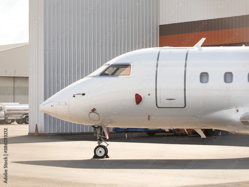 The nose of an unidentified private business jet parked at an airport hangar The nose of an unidentified private business jet parked at an airport hangar