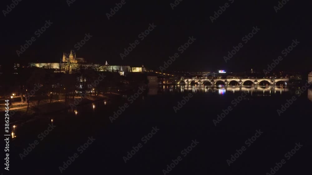 A scenic view of Charles bridge in the historical centre of Prague, Czechia, over the Vltava river at night, during a Covid-19 lockdown, city and Prague castle lit by street lamps, scenic pan shot. A scenic view of Charles bridge in the historical centre of Prague, Czechia, over the Vltava river at night, during a Covid-19 lockdown, city and Prague castle lit by street lamps, scenic pan shot.