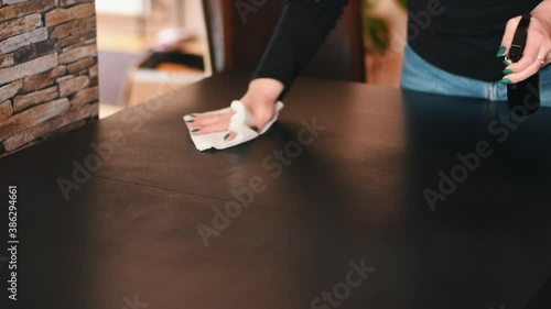 Woman with painted nails disinfects a black table with disinfectant spray - Warm tones photo