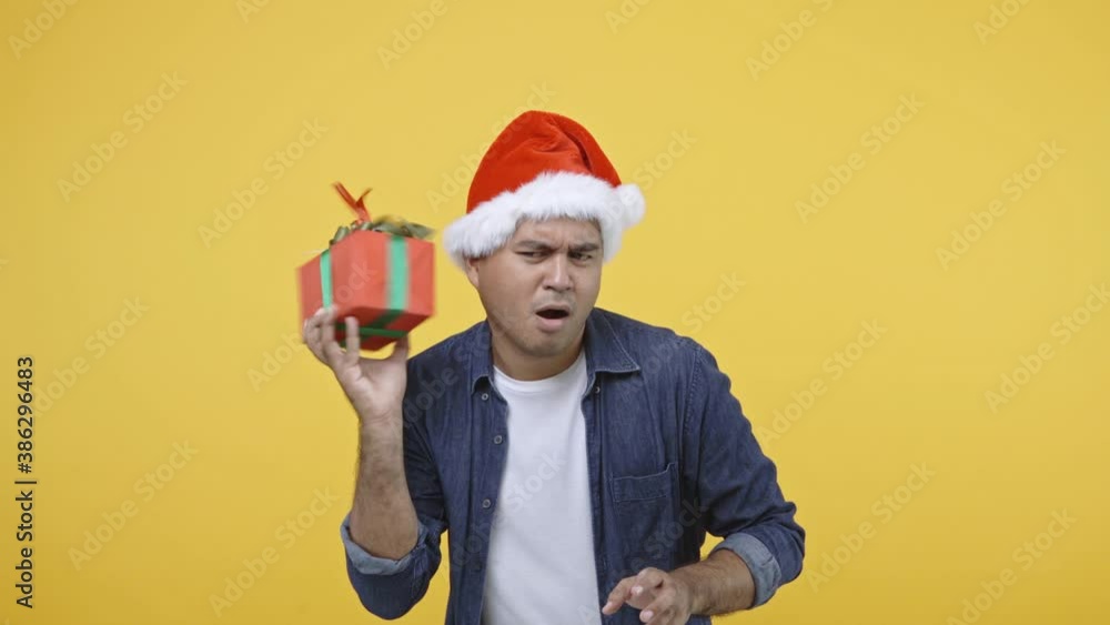 Funny asian man shaking the gift box he want to know what thing is inside the box. He face very confused. Happy christmas theme concept. 4K Resolution. Funny asian man shaking the gift box he want to know what thing is inside the box. He face very confused. Happy christmas theme concept. 4K Resolution.