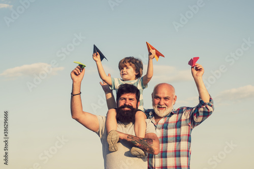 Grandfather with son and grandson having fun in park. Happy child playing with toy paper airplane against summer sky background. Child happy. Enjoy family together.
