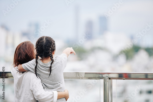 Mother and little daughter standing on observation platform and looking at the city