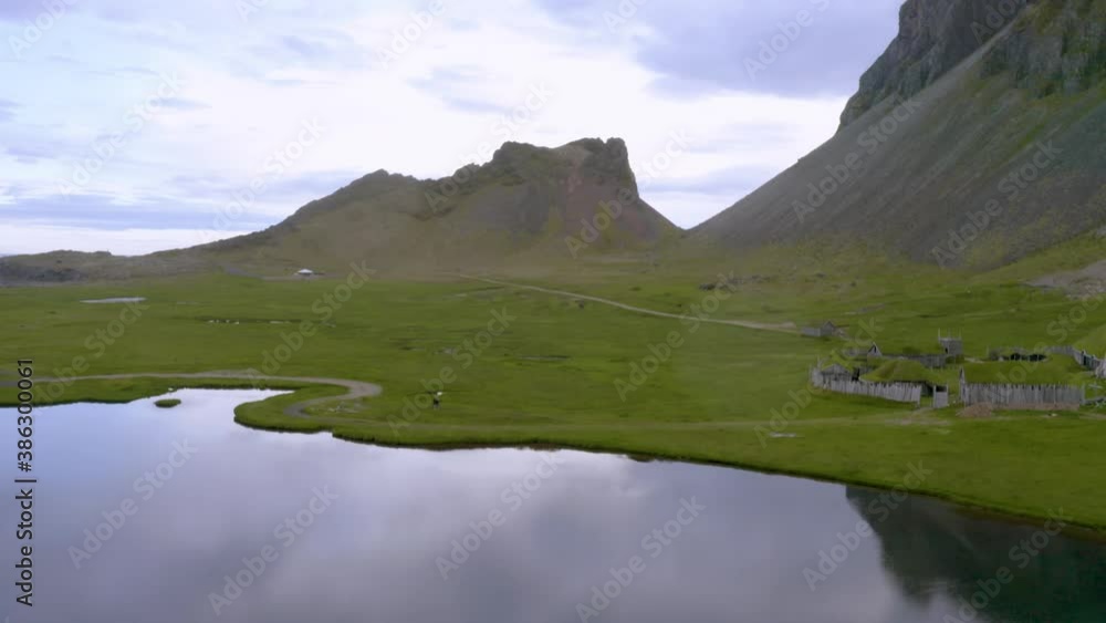 Forward moving aerial over the calm lake amidst green valley all surrounded by steep mountains on a cloudy day, Iceland. Forward moving aerial over the calm lake amidst green valley all surrounded by steep mountains on a cloudy day, Iceland.
