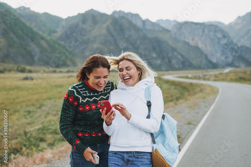 Happy young women travellers using mobile on road against the beautiful mountain landscape