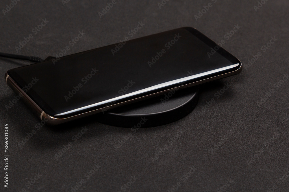 Wireless charging for phone on black background. Smartphone charges on fast induction charger. Wireless charging for phone on black background. Smartphone charges on fast induction charger.