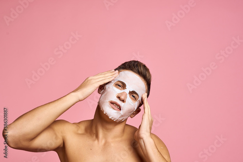 man with cleansing mask against black dots on his face on pink background cropped view and hands near face