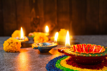 Close up clay lit light a fire already on Diya or oil lamp with flowers on concrete background, Decoration of Hinduism rangoli, Happy celebration Deepavali, or Diwali Indian festival concept