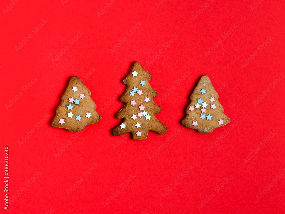 Gingerbread christmas trees cookie decorated with mastic star icing on bright red background. Festive, holiday cooking concept.