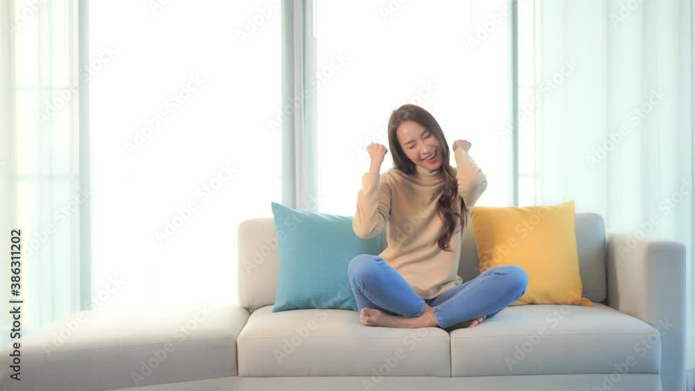 A young woman sitting on a couch expresses her enthusiasm by thrusting her arms in the air with joy. A young woman sitting on a couch expresses her enthusiasm by thrusting her arms in the air with joy.