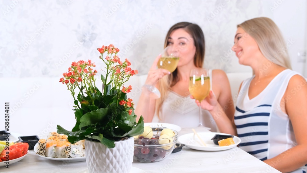 Two attractive girls, cheerful best friends having fun and drinking wine at home. Two glasses of white wine in hands. Girls having fun time together gossiping. Two attractive girls, cheerful best friends having fun and drinking wine at home. Two glasses of white wine in hands. Girls having fun time together gossiping.