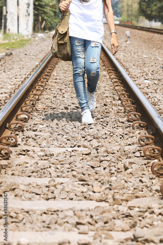 girl walking in railroad wearing ripped jeans, sling bag, white tees, sneakers, hipster style, casual, clothes for youth, no face, lower part of body, sporty style.