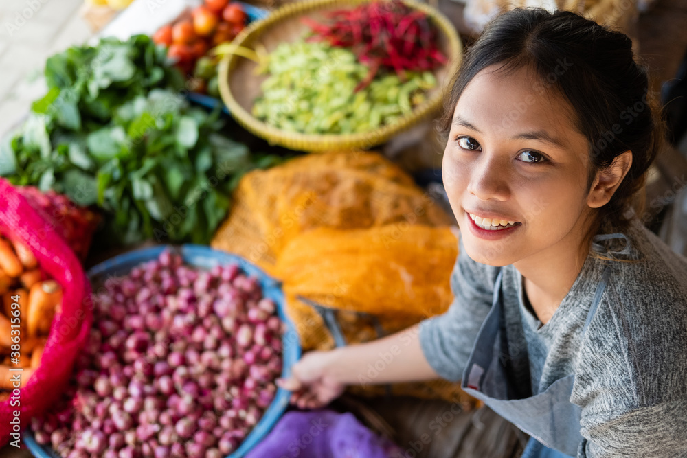 top side view of a beautiful Asian greengrocer holding a tray at a vegetable stall