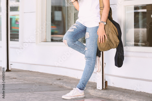 girl wearing ripped jeans, sling bag, white tees, sneakers, hipster style, casual, clothes for youth, no face, lower part of body, sporty style. photo