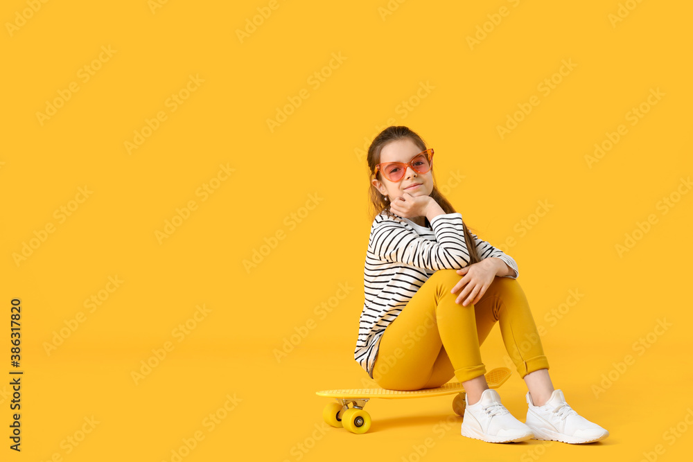 Fototapeta premium Cute little girl with skateboard on color background