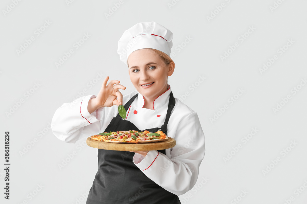 Mature female chef with tasty pizza on grey background Mature female chef with tasty pizza on grey background