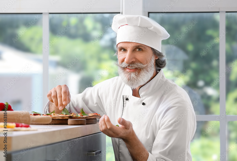 Mature male chef with tasty pizza in kitchen Mature male chef with tasty pizza in kitchen