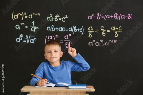 Cute pupil with raised index finger sitting at desk during lesson in classroom