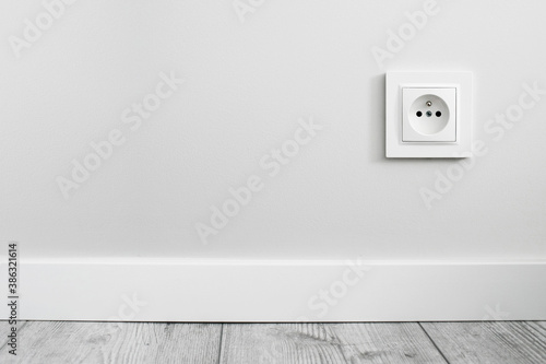 Electrical socket isolated on gray wall. Renovated studio apartment power supply background. Empty copy space single white plastic power outlet. photo