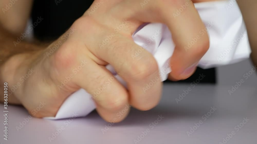 An angry man crumples a sheet of paper in his hand and puts it on the white table close-up An angry man crumples a sheet of paper in his hand and puts it on the white table close-up
