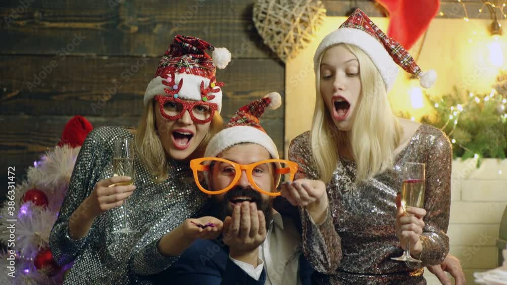 Happy friends having christmas at home, drinking wine and clinking glasses. Funny people wearing red Santa hat. Group of young friends having fun at New Years Eve Party. Happy friends having christmas at home, drinking wine and clinking glasses. Funny people wearing red Santa hat. Group of young friends having fun at New Years Eve Party.