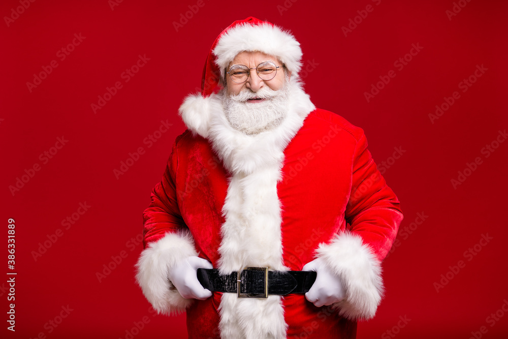 Photo of retired old man grey beard hand hip cheerful self-assured wait last days before newyear wear santa costume leather belt gloves coat spectacles headwear isolated red color background
