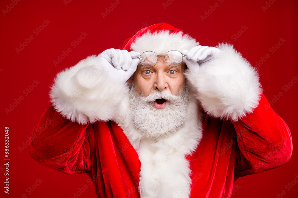 Photo of pensioner old man grey beard excited look hold eyeglasses open mouth shock see female same outfit wear santa costume coat spectacles headwear isolated red color background Photo of pensioner old man grey beard excited look hold eyeglasses open mouth shock see female same outfit wear santa costume coat spectacles headwear isolated red color background