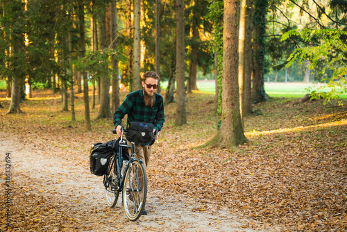 Hipster man pushing a bicycle at a public park during autumn.