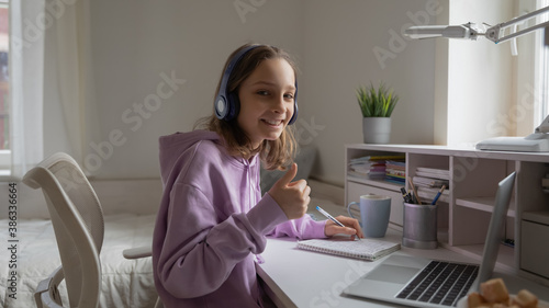 Portrait of smiling teenager in earphones look at camera show thumb up recommend distant education. Happy teen girl pupil in headphones give recommendation to online web studying from home.