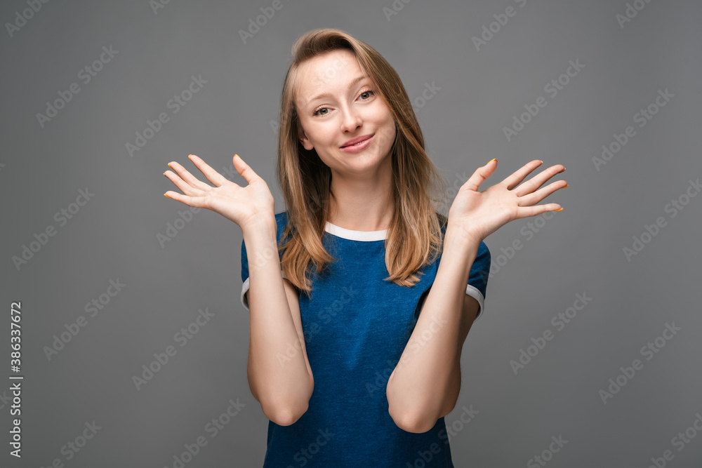 Positive Young female is smiling happily and spreads her hands to the side. Human emotions, facial expression concept. Positive Young female is smiling happily and spreads her hands to the side. Human emotions, facial expression concept.