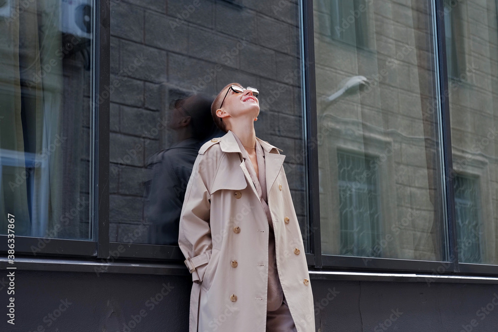 A woman with short hair in gray coat and glasses dancing, walking, smiling on a city street.